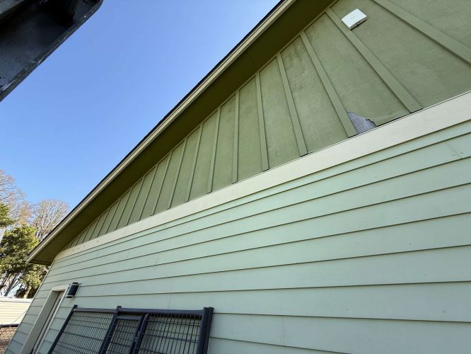 Close-up of exterior wall damage on a light green building with vertical and horizontal siding in Portland, photographed by painter McCaffery for Pearl Painters in April 2025.