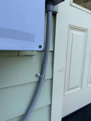 A gray electrical conduit is attached to a green exterior wall near a white door and utility box—exterior painting work by McCaffery, painter, in Portland, April 2025. Pearl Painters.