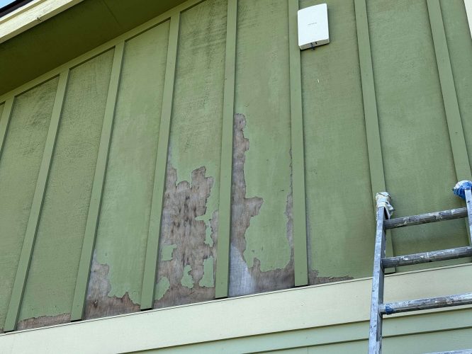 Close-up of a green exterior wall in Portland with peeling paint and exposed wood, next to a metal ladder and white utility box. Photo taken by painter McCaffery for Pearl Painters, April 2025.