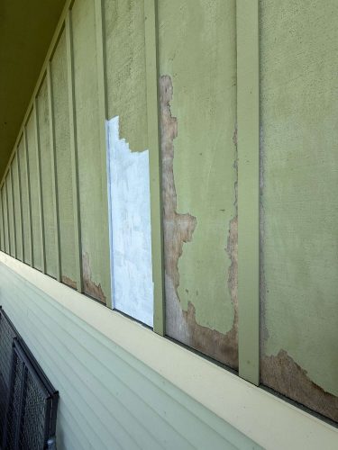 A painter from Pearl Painters in Portland prepped an exterior wall for a McCaffery project in April 2025; green paint is peeling to reveal brown areas, with one section covered in fresh white primer.