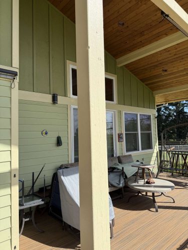 Exterior view of a covered porch in Portland with light green siding and wooden ceiling, painted by Pearl Painters; shows tables and McCaffery furniture stacked in sunlight, April 2025.