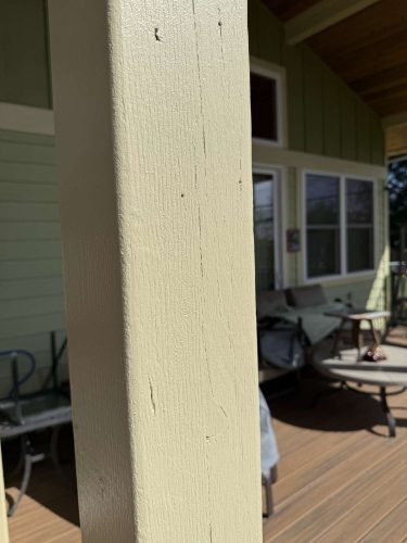 A beige wooden porch post painted by Pearl Painters, a Portland painting company. Patio furniture, green siding, and large windows are in the background.