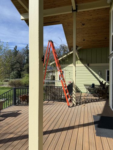 A red step ladder stands on the wooden deck of a yellow house with a slanted roof in Portland, photographed in April 2025. This painting by Pearl Painters captures a typical scene for any local painter.
