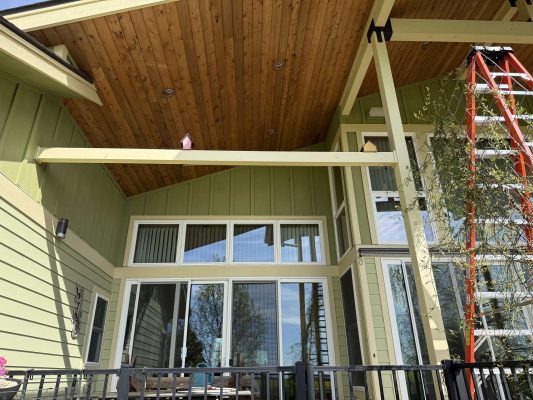 Exterior view of a green house in Portland with large windows, vaulted wooden patio ceiling, and a red extension ladder visible. Photo by painter McCaffery for Pearl Painters, April 2025.