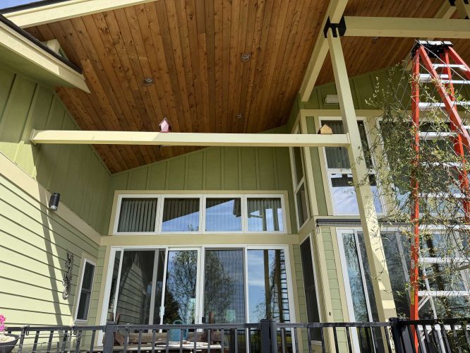 Exterior view of a green house in Portland with large windows, vaulted wooden patio ceiling, and a red extension ladder visible. Photo by painter McCaffery for Pearl Painters, April 2025.