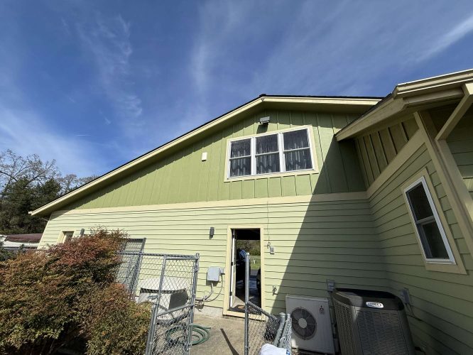 Pearl Painters completed a green exterior painting with light siding on a McCaffery building in Portland. The building has two upper windows, a lower door, and outdoor HVAC units with fencing in front.