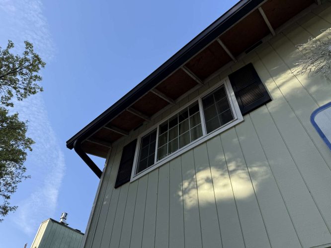 A light green house exterior with black shutters and a large window, painted by Wehage of Pearl Painters in Portland, photographed in April 2025.