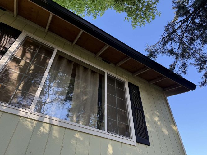 Exterior view of a house window with black shutters, painted by Pearl Painters in Portland, April 2025. Tree branches and blue sky are visible.