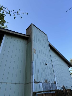 Photographed by Wehage in April 2025, this image shows a light blue exterior wall with water damage, peeling paint, and patchwork repairs. Painters in Portland, such as Pearl Painters, could address these issues.