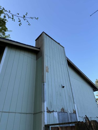 Photographed by Wehage in April 2025, this image shows a light blue exterior wall with water damage, peeling paint, and patchwork repairs. Painters in Portland, such as Pearl Painters, could address these issues.