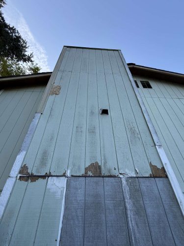 A building’s tall, weathered exterior wall in Portland, with peeling paint and a small vent, photographed in April 2025. Pearl Painters recommends repainting by a professional painter.