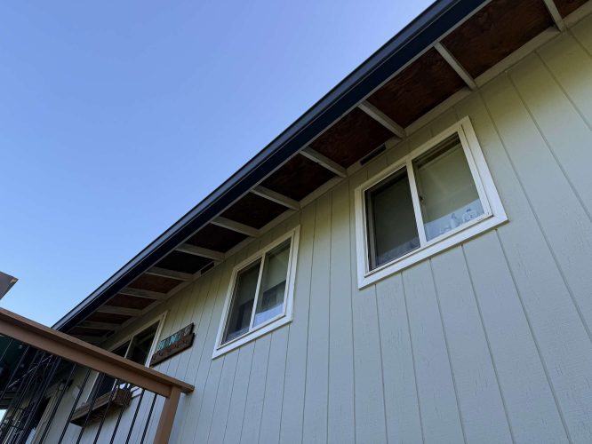 View of a light-colored Wehage house in Portland with two windows and exposed rafters, painted by Pearl Painters.