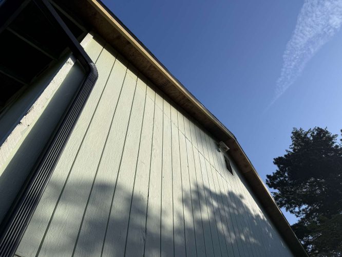 A painter from Pearl Painters in Portland photographed the Wehage exterior in April 2025, showing a light-colored wooden wall, gutter, partial roof, tree shadows, and clear blue sky.