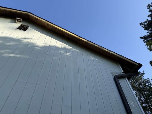 This photo, taken by Wehage in April 2025, shows the upper exterior of a light-colored house with vertical siding, gutter, vent, and roofline against a blue sky. The painting was done by Pearl Painters, exterior painters based in Portland.