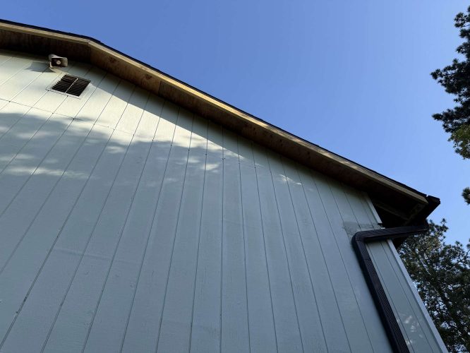 This photo, taken by Wehage in April 2025, shows the upper exterior of a light-colored house with vertical siding, gutter, vent, and roofline against a blue sky. The painting was done by Pearl Painters, exterior painters based in Portland.