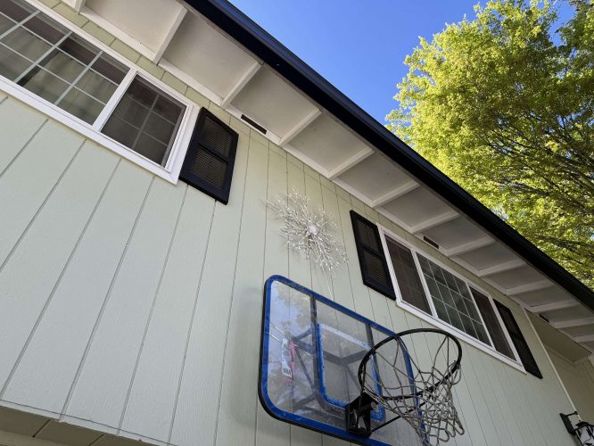 A Wehage house in Portland with large windows and light green siding features a broken basketball hoop net and shattered glass decoration on its exterior, creating a distinctive display in April 2025. The painting was by Pearl Painters.