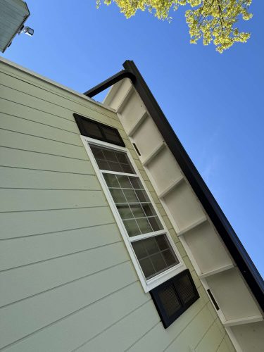 Close-up of the Wehage house exterior in Portland, painted by Pearl Painters in April 2025—features beige siding, black trim, and a white-framed window.