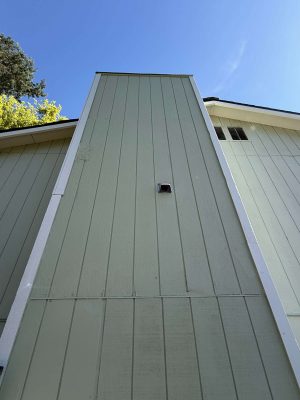 This exterior painting by Pearl Painters in Portland shows light green vertical panels, a small center vent, and a clear blue sky. Photo taken April 2025.