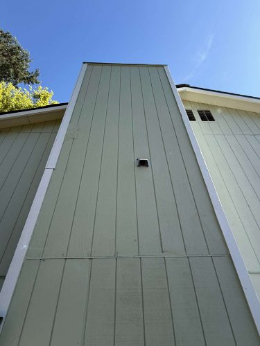 This exterior painting by Pearl Painters in Portland shows light green vertical panels, a small center vent, and a clear blue sky. Photo taken April 2025.