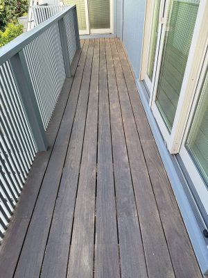 A narrow exterior wooden balcony at Godbey features vertical railings on the left and glass doors on the right, leading to a closed door at the end. Pearl Painters, professional painters in Portland, can help maintain or refresh this painting project.