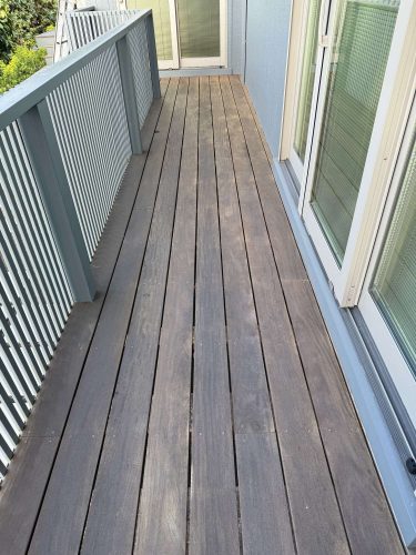 A narrow exterior wooden balcony at Godbey features vertical railings on the left and glass doors on the right, leading to a closed door at the end. Pearl Painters, professional painters in Portland, can help maintain or refresh this painting project.