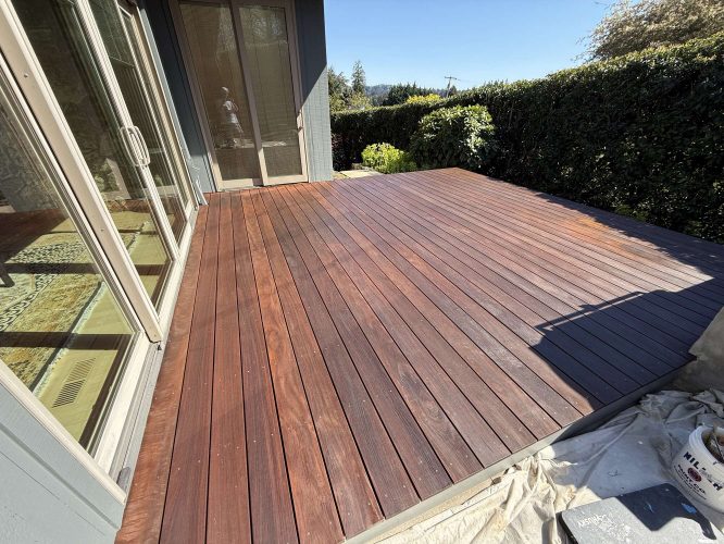 A wooden deck outside a Portland home is partially shaded, with sunlight on the wood grain. A drop cloth is laid out nearby. Pearl Painters will update this exterior in April 2025.