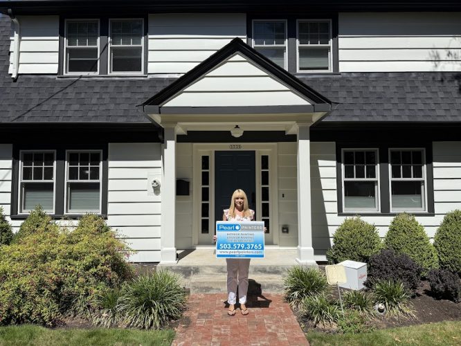 Woman on brick walkway in front of white house displays Pearl Painters sign—exterior painting, Portland, 503-579-3765.