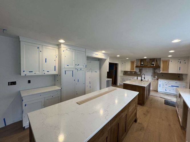 Modern kitchen under construction in Portland: white Evans cabinets, blue painter’s tape on doors and drawers, two islands with white marble countertops, unfinished details. Pearl Painters involved.