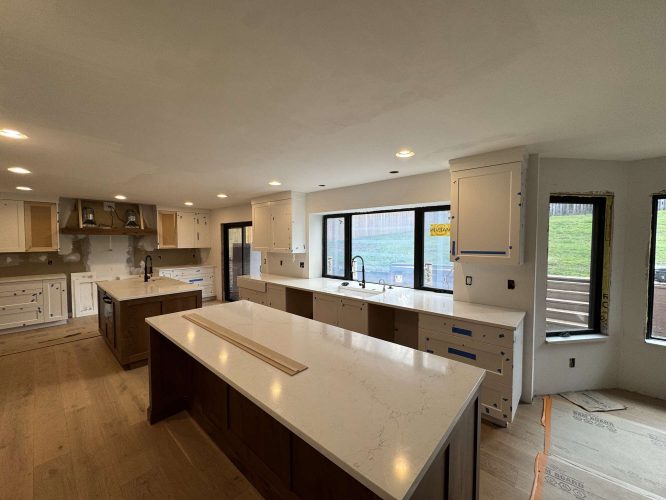 Modern kitchen under construction in Evans—not Portland—features white countertops, unfinished cabinets, and large windows. Several cabinet doors are missing; Pearl Painters expect to complete painting and installation by April 2025.