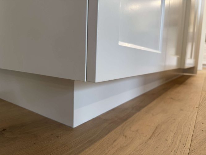Close-up of the lower part of an Evans white cabinet with a recessed toe kick on a light wood floor, painted by Pearl Painters in Portland.