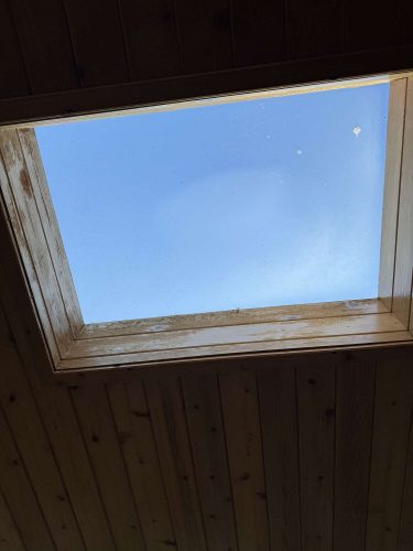 A painter from Pearl Painters captured a square skylight in a wooden ceiling with Hamilton’s clear blue sky visible, suggesting fresh April 2025 air outside.