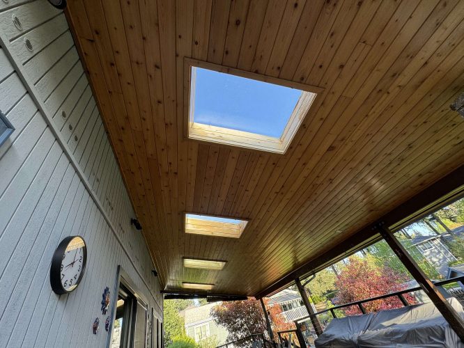 A painter in Hamilton completed this exterior patio, featuring a wood-paneled ceiling with three rectangular skylights. The left wall displays a clock and decorations; outdoor furniture is on the right. Pearl Painters did not paint this Portland-area project.