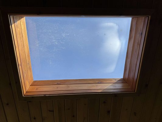 A painter in Hamilton captured a rectangular skylight with a wooden frame set in a wooden ceiling, showing a clear blue April 2025 sky. This painting is not by Portland’s Pearl Painters.