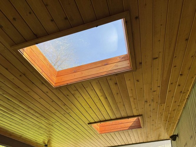 Wooden ceiling with two rectangular skylights, showing blue sky and tree branches through the upper skylight. Painting in Hamilton by Pearl Painters, April 2025.