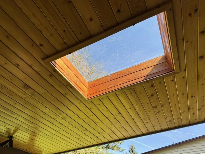 A square skylight in the wooden ceiling lets sunlight and views of tree branches and the April 2025 sky into a Hamilton home, connecting interior and exterior. Pearl Painters, Portland painters, completed the painting.