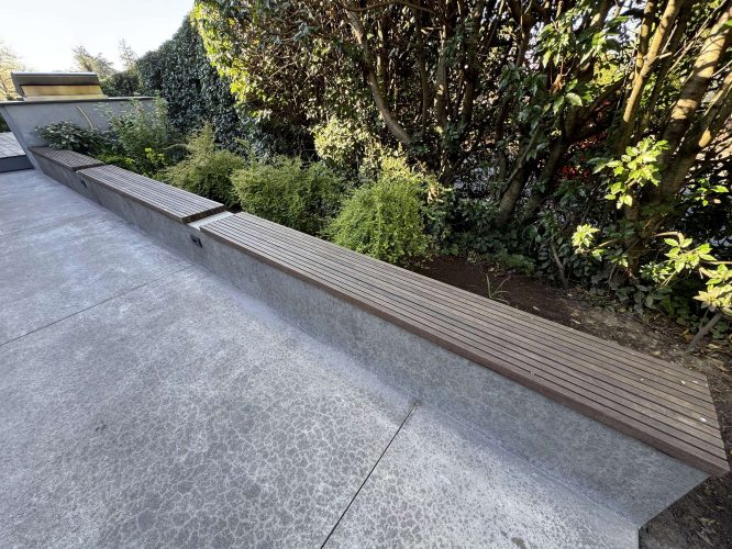 Pearl Painters, a Portland painting company, will work on the Godbey project in April 2025, which features a long wooden bench with a concrete base along the edge of a paved outdoor area near shrubs and trees.