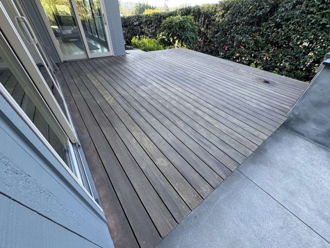 A wooden deck next to a modern house with glass doors and greenery, plus an adjacent concrete area, was painted by Pearl Painters in Portland for April 2025.