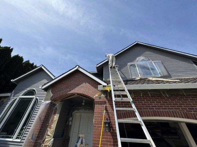 Scott, a painter with Pearl Painters, paints the exterior of a two-story brick and siding house in Portland in April 2025.
