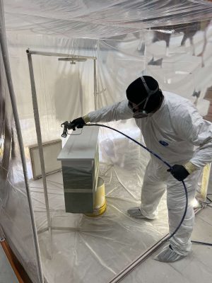 A painter from Pearl Painters in Portland spray paints white cabinets inside a plastic enclosure, prepping them for installation by Evans in April 2025.