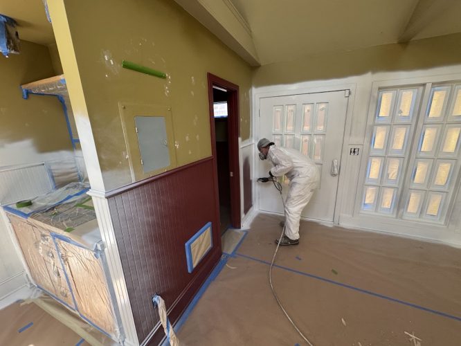 Pearl Painters' painter Dennis sprays white paint on a door frame in a prepped Portland room, July 2025.