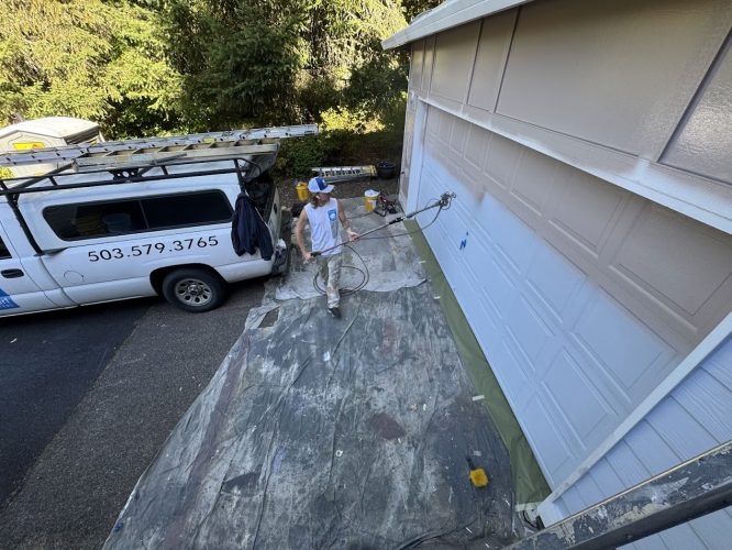 Painter uses spray gun on garage door and siding near white van, Pearl Painters, Anderson project, Portland, August 2025.