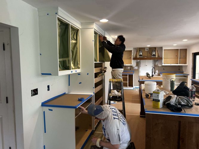 Two Evans painters are painting kitchen cabinets in a renovated kitchen, with protective tape and coverings visible; location is not specified as Portland.