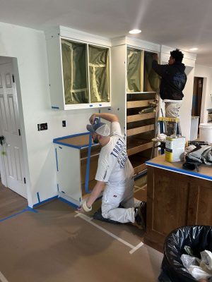 Two Evans painters are prepping a kitchen for painting in Portland, taping off surfaces and covering cabinets.