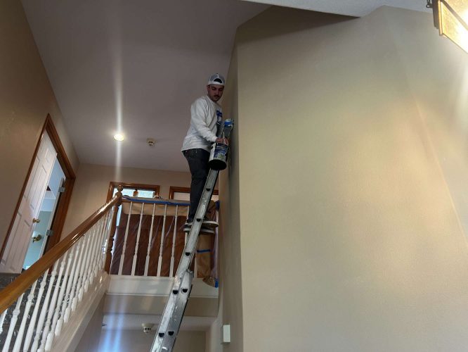 Painter Mann of Pearl Painters paints a high interior wall near the staircase in Portland, preparing the house for a fresh look in April 2025.