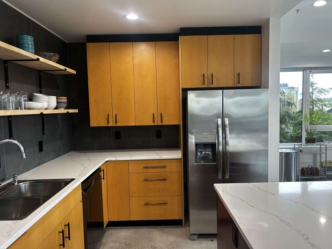 Modern kitchen in Portland with Isadore wood cabinets, stainless steel refrigerator, open shelves, and marble countertops under recessed lighting. Painted by Pearl Painters in April 2025.