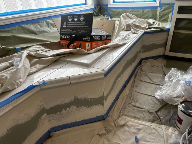 In April 2025, a painter from Pearl Painters in Portland worked on an interior kitchen countertop that was under construction, partially tiled, covered with protective sheets and painter's tape, with Mallen power tool boxes present.