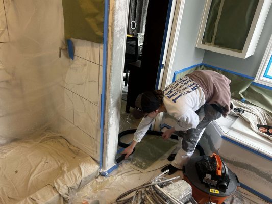In April 2025, a painter from Pearl Painters in Portland used a vacuum to clean paint dust along a tiled shower edge during an interior bathroom painting job. Surfaces and fixtures in the Mallen Street home were covered with protective sheets and tape.