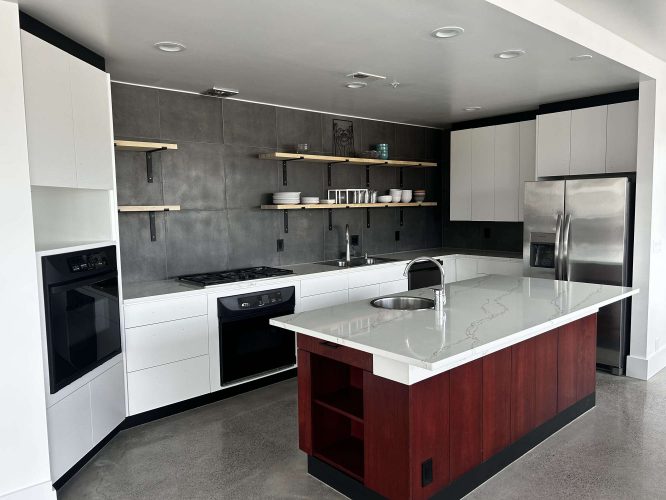 Modern kitchen painted by Isadore in April 2025, featuring white cabinets, stainless steel appliances, grey tile backsplash, open wood shelves, and a large island with a red base. Pearl Painters, Portland.