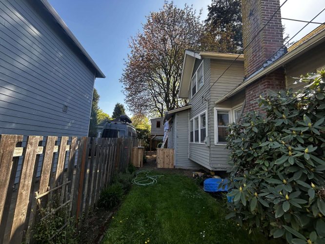 Pearl Painters documented this Portland exterior painting project in April 2025: a beige house with a brick chimney, fenced backyard, green grass, large shrub, and nearby Airstream trailer.