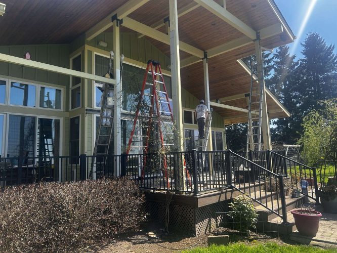 In April 2025, two painters work on ladders painting or repairing the exterior columns of a McCaffery house with large windows and a wooden porch in Portland. Pearl Painters is involved.